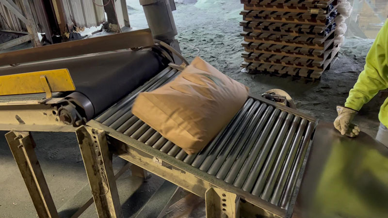 50 lb paper bags of abrasive sand on gravity roller conveyor for palletizing