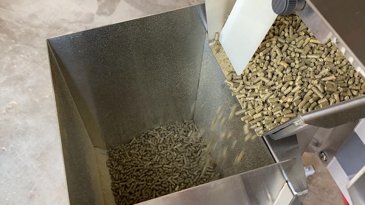 Mini feed pellets flowing into weigh hopper from vibrating feeder