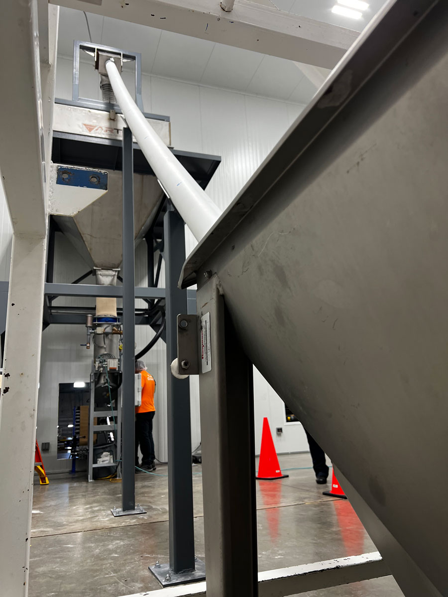 Flexible screw conveyor elevates and discharges granulated sugar into surge hopper