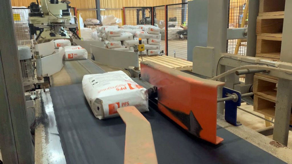 50 lb craft paper valve bags conveyed past lot code printing head toward robotic palletizer