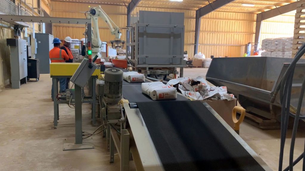 50 lb valve bags of silica sand conveyed across check weigher toward robotic palletizer
