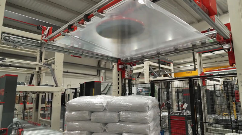 stretch hooding system applying top fitted plastic sleeve to pallet of bags