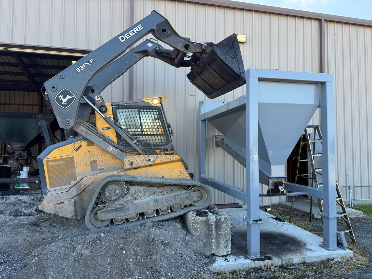 skid steer loader dumping asphalt cold patch into surge hopper