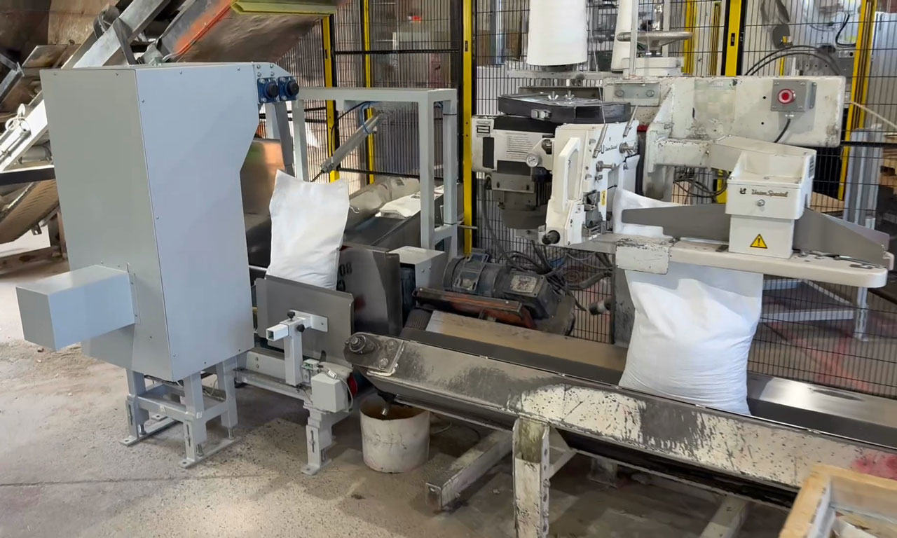 bags of premix concrete moving through bag sewing system and then into bag kicker conveyor