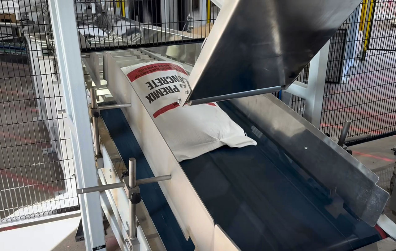 filled bag of premix concrete moving from kicker to square roller conveyor